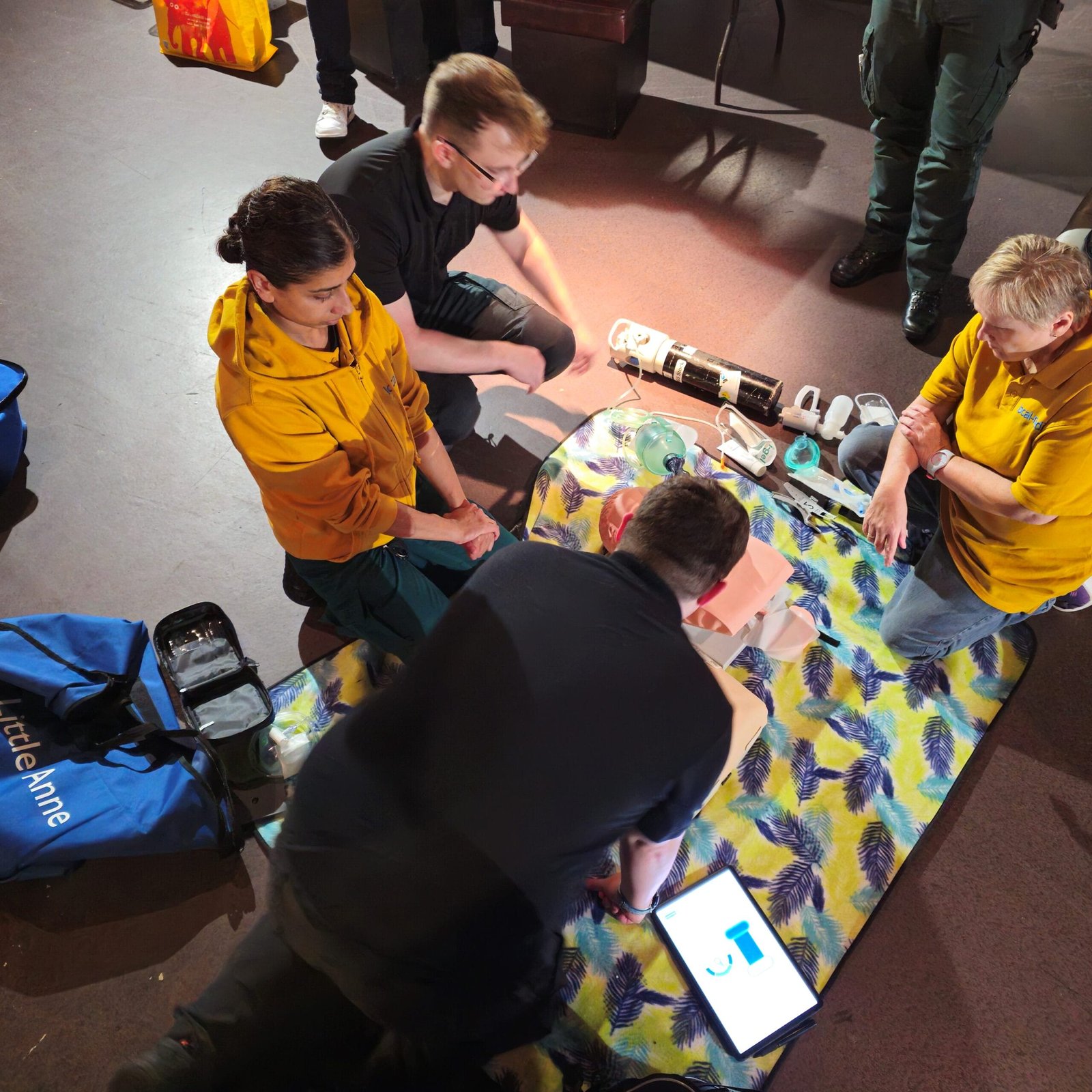 People practicing CPR on a dummy, surrounded by medical equipment and a colorful blanket.