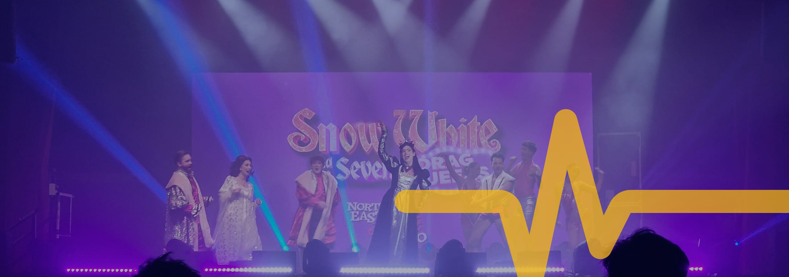 Seven performers in costume stand on stage under bright lights with a “Snow White and the Seven Drag Queens” backdrop; a large yellow graphic overlays the image. - on localmedic
